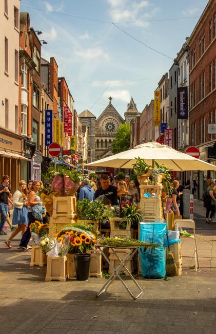 A bustling street scene on Church Road in Upper Norwood, featuring a flower stall operated by flowersuppernorwood.co.uk. The display includes a variety of fresh flowers such as sunflowers, roses, and 